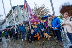 Leonie Winter und Otto Steinkamp (vorn auf der Bank) hissen gemeinsam mit zahlreichen Gästen die Flagge gegen Gewalt an Frauen. Foto: André Thöle / Gemeinde Wallenhorst