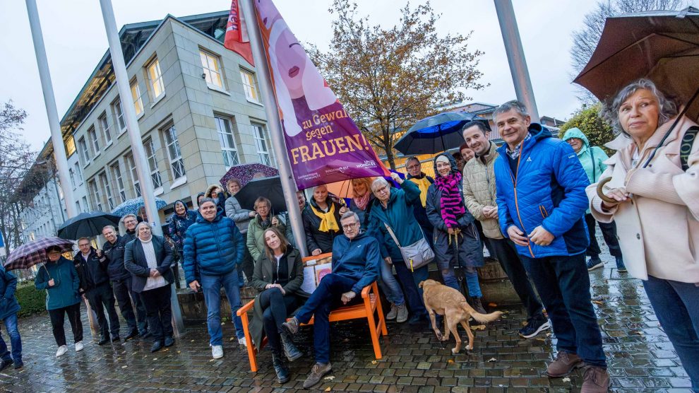 Leonie Winter und Otto Steinkamp (vorn auf der Bank) hissen gemeinsam mit zahlreichen Gästen die Flagge gegen Gewalt an Frauen. Foto: André Thöle / Gemeinde Wallenhorst